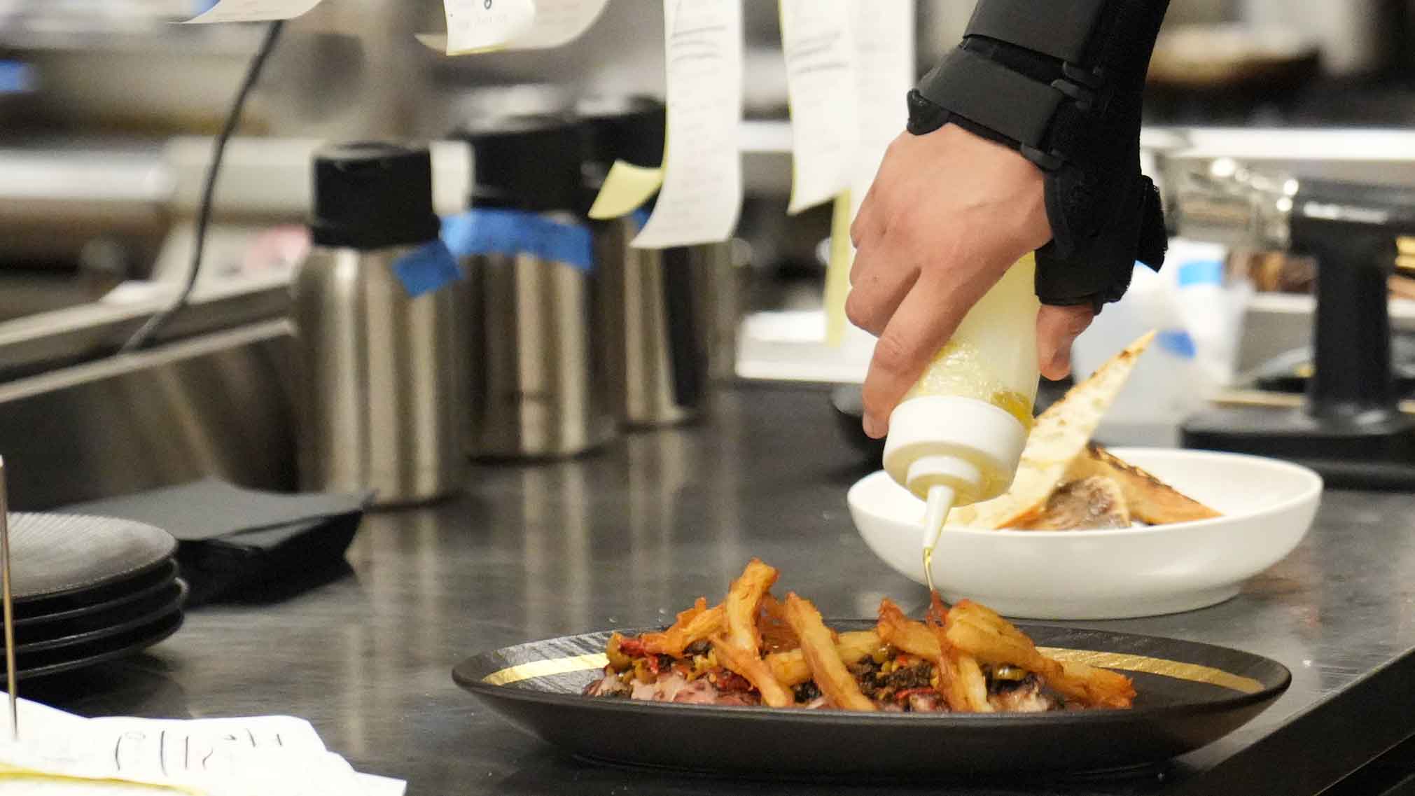 A chef finishing dishes at the Braseria kitchen pass