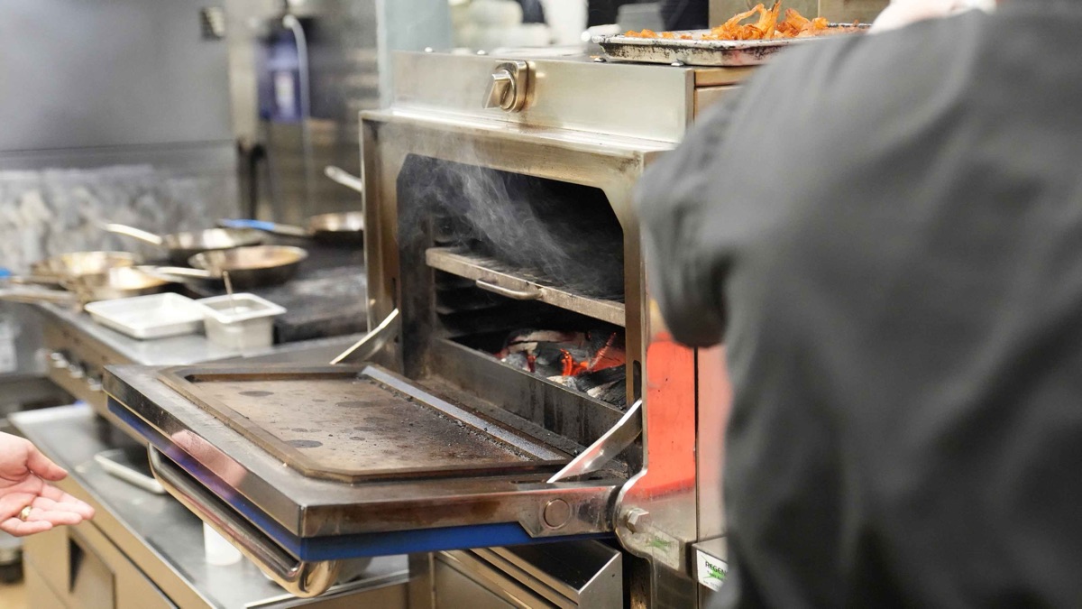 A cook working the wood-fired Mibrasa oven in the Braseria by EDO kitchen.